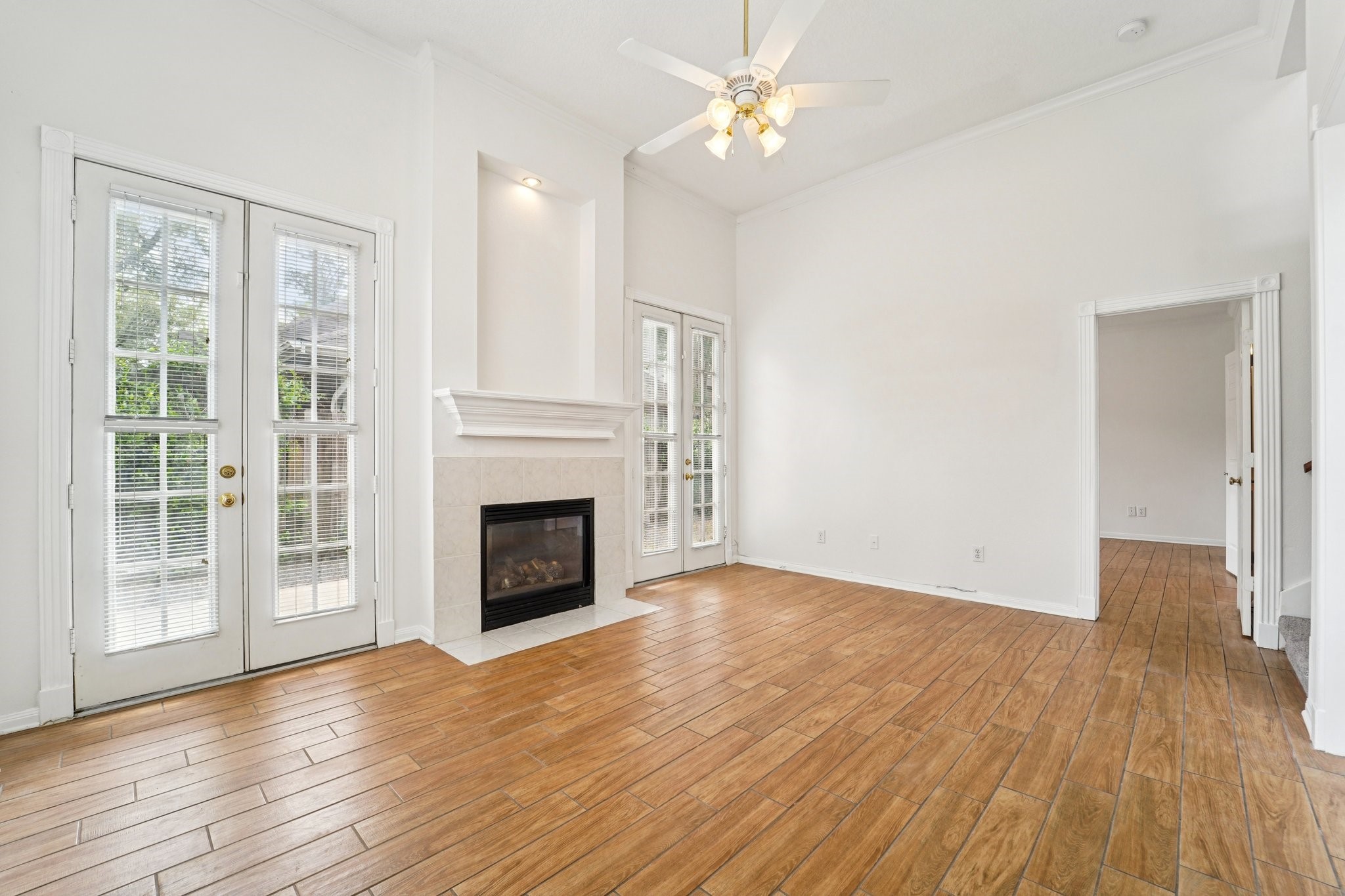 14420 Walters Road, Unit 55 Houston, TX 77014 - Photo 4 of 35 Bright living room with high ceilings, a ceiling fan, and wood-style flooring. It features a cozy fireplace and large French doors leading to the outside, offering ample natural light.