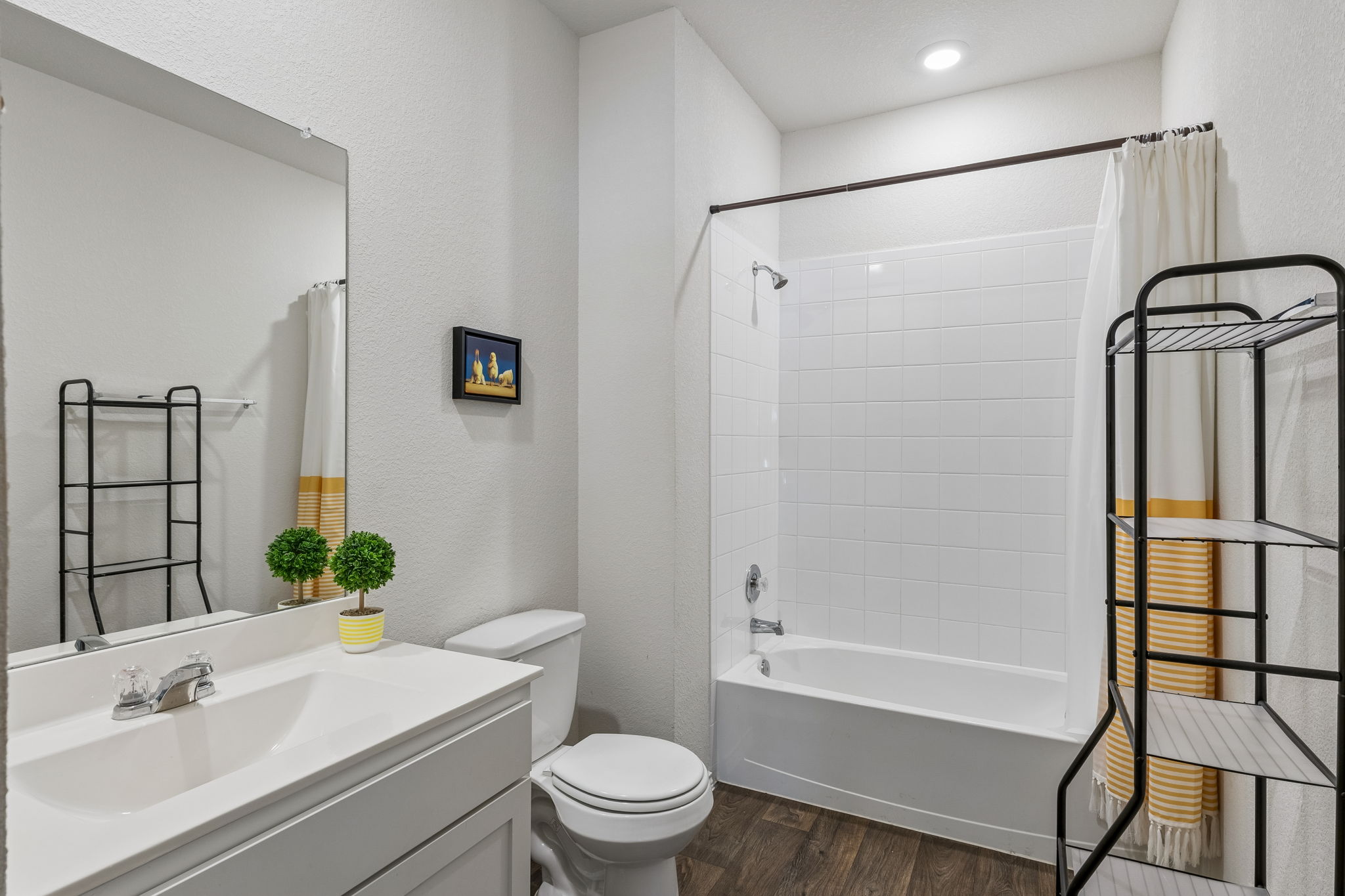 343 Sickle Loop Kyle, TX 78640 - Photo 5 of 40 Bathroom featuring wood-finish flooring, a white vanity with an integrated sink, a built-in bathtub with subway tile surround, and a toilet