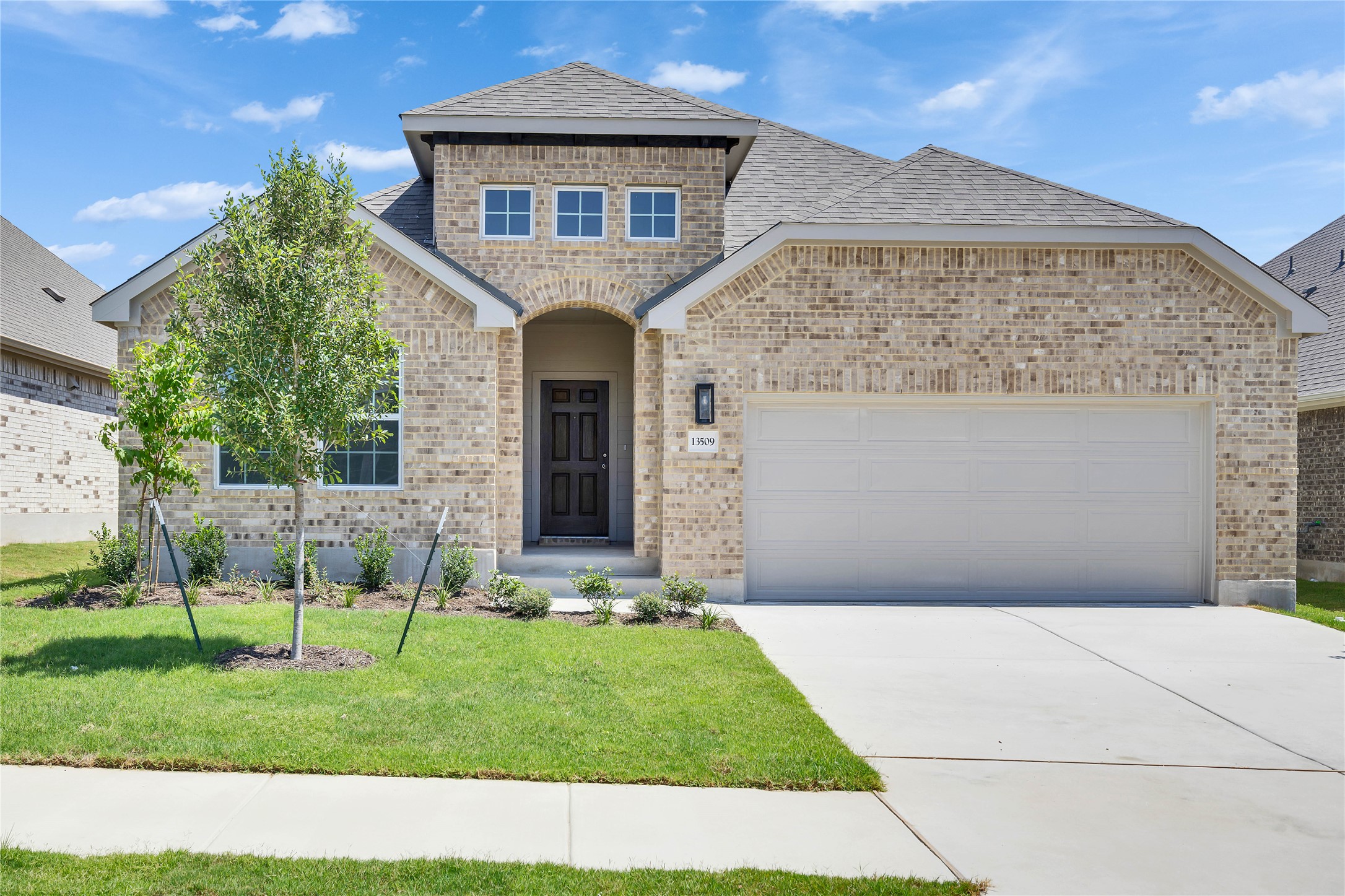 French provincial home with brick siding, a front yard, a shingled roof, and concrete driveway