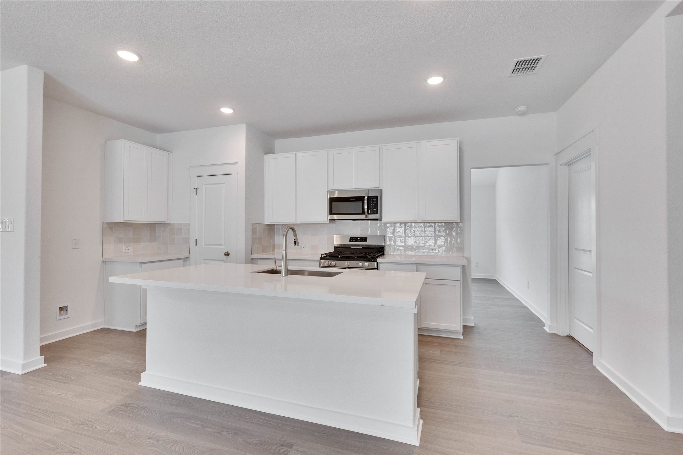 13509 Barn Chime Street Elgin, TX 78621 - Photo 20 of 30 Kitchen featuring tasteful backsplash, white cabinets, appliances with stainless steel finishes, a center island with sink, and light wood-type flooring