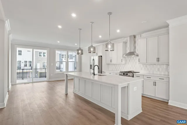 a large kitchen with stainless steel appliances kitchen island granite countertop a stove a sink a refrigerator and white cabinets with wooden floor