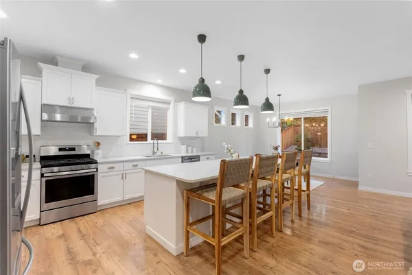 a kitchen with stainless steel appliances kitchen island granite countertop a stove a sink a refrigerator a dining table and chairs with wooden floor