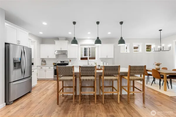 a kitchen with stainless steel appliances granite countertop a dining table chairs refrigerator and sink