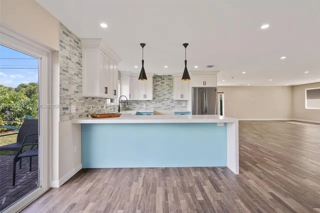 a large kitchen with stainless steel appliances a large counter top a wooden floors and a large window