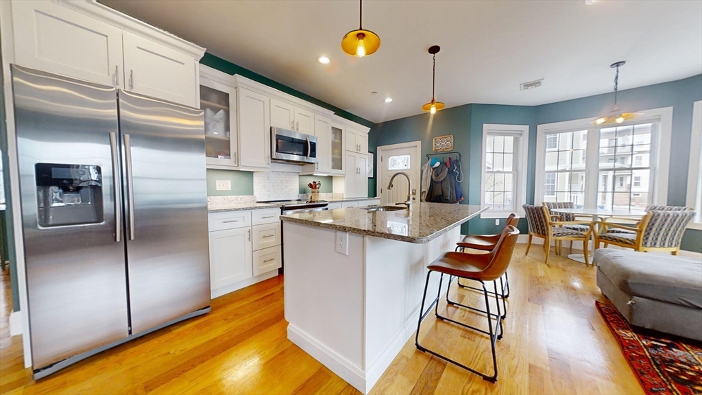 42 Olney Street, Unit 1R Boston, MA 02121 - Photo 9 of 21 a kitchen with stainless steel appliances kitchen island granite countertop a refrigerator a stove a dining table and chairs with wooden floor