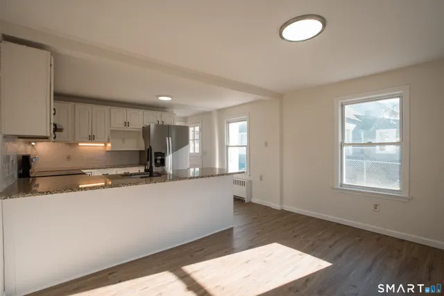 a large kitchen with stainless steel appliances granite countertop a stove a sink a refrigerator and white cabinets with wooden floor