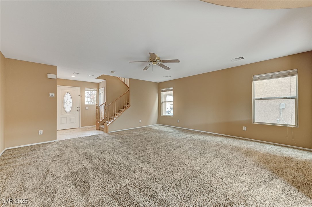 83 Lockheed Avenue Las Vegas, NV 89183 - Photo 4 of 28 Unfurnished living room featuring light colored carpet, stairway, plenty of natural light, and ceiling fan