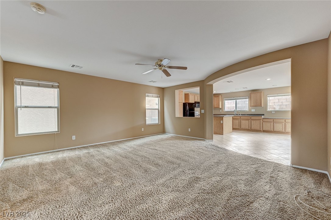 83 Lockheed Avenue Las Vegas, NV 89183 - Photo 5 of 28 Unfurnished living room with light colored carpet, a ceiling fan, arched walkways, and light tile patterned floors