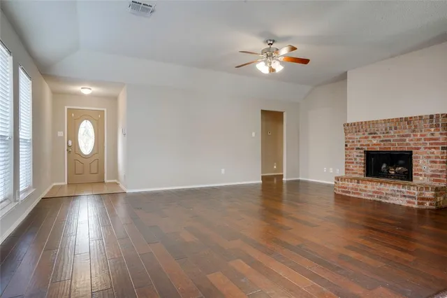 an empty room with wooden floor fireplace and windows