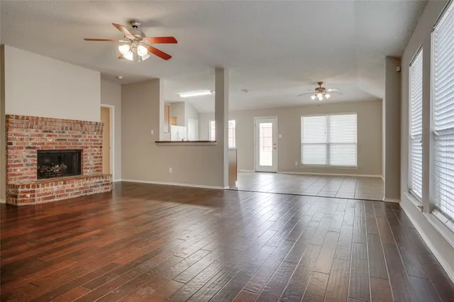 an empty room with wooden floor fireplace and windows