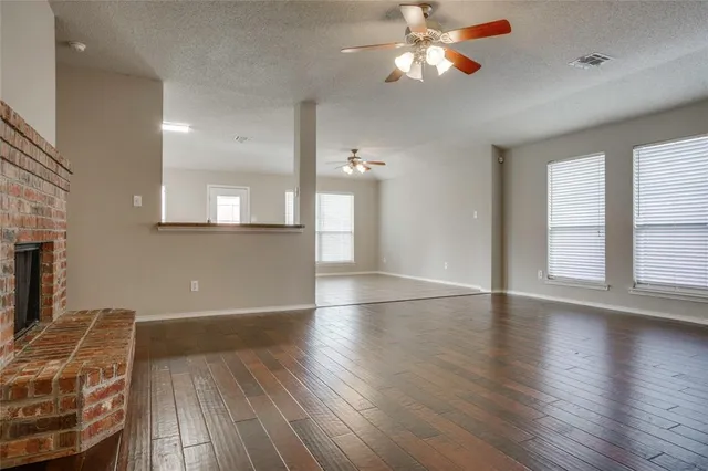 an empty room with wooden floor chandelier fan and windows