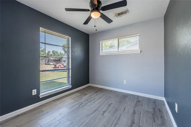 an empty room with wooden floor chandelier fan and windows