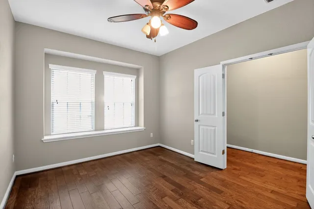 an empty room with wooden floor chandelier fan and windows