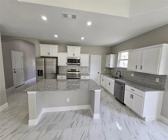 a large kitchen with granite countertop a large counter top stainless steel appliances and cabinets