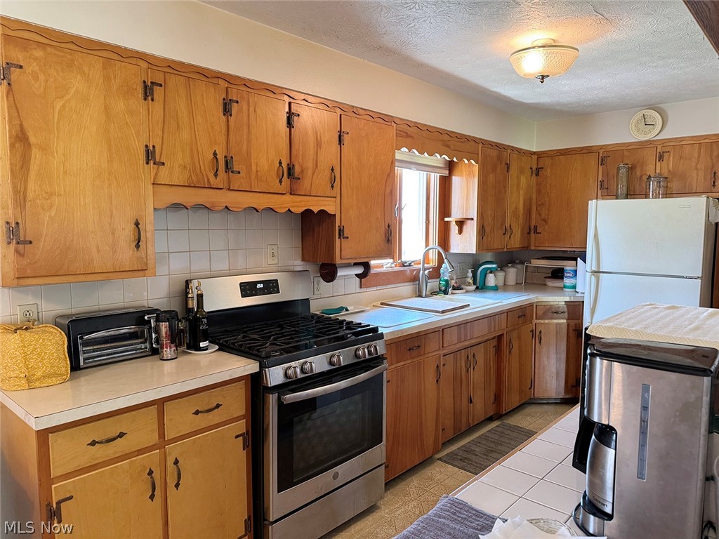 5934 Ryan Road Medina, OH 44256 - Photo 6 of 24 Kitchen with gas range, white refrigerator, light tile floors, tasteful backsplash, and a textured ceiling
