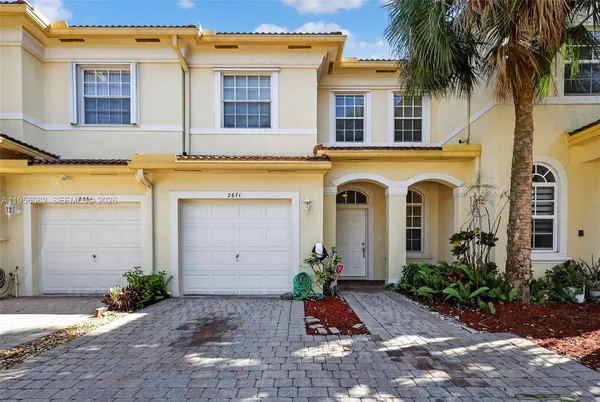 a view of a white house with potted plants and a large tree