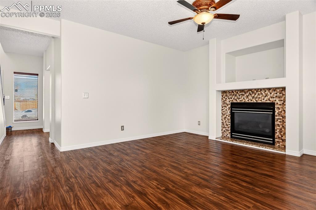 7763 Middle Bay Way Fountain, CO 80817 - Photo 8 of 44 an empty room with wooden floor a fireplace a ceiling fan and a window