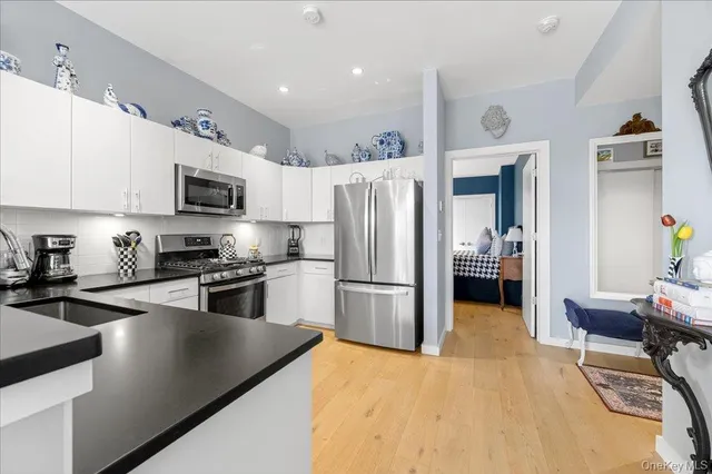 a kitchen with a refrigerator a stove top oven a sink dishwasher and white cabinets with wooden floor