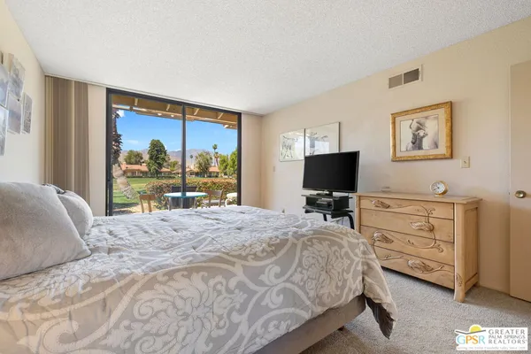 a spacious bedroom with a bed and a flat tv screen on dresser