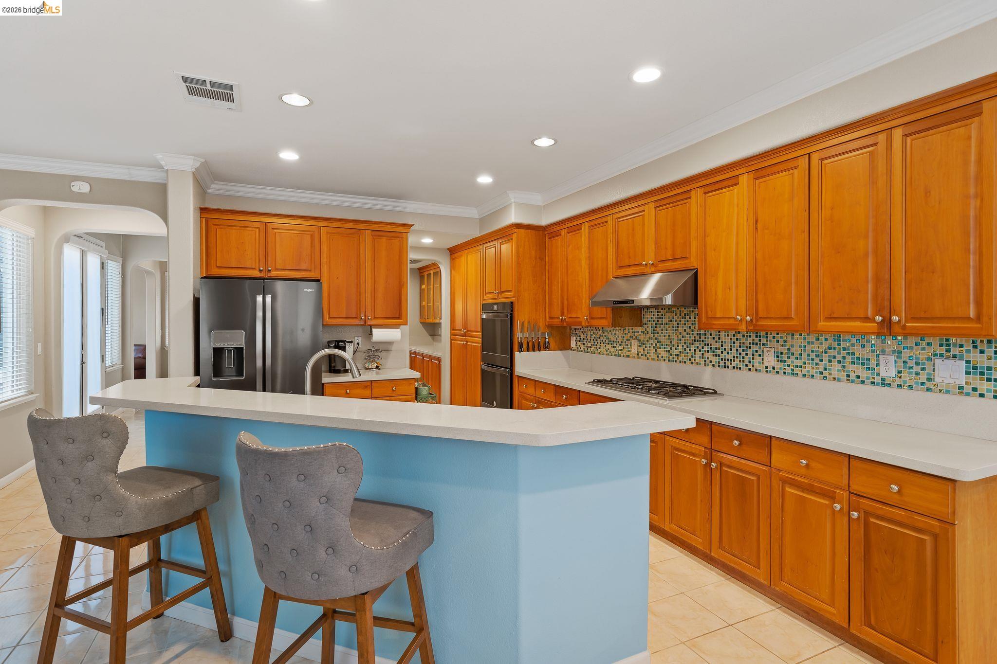 3237 Oso Grande Way Antioch, CA 94531 - Photo 15 of 47 Kitchen with arched walkways, backsplash, a kitchen breakfast bar, stainless steel appliances, and wood finish cabinets
