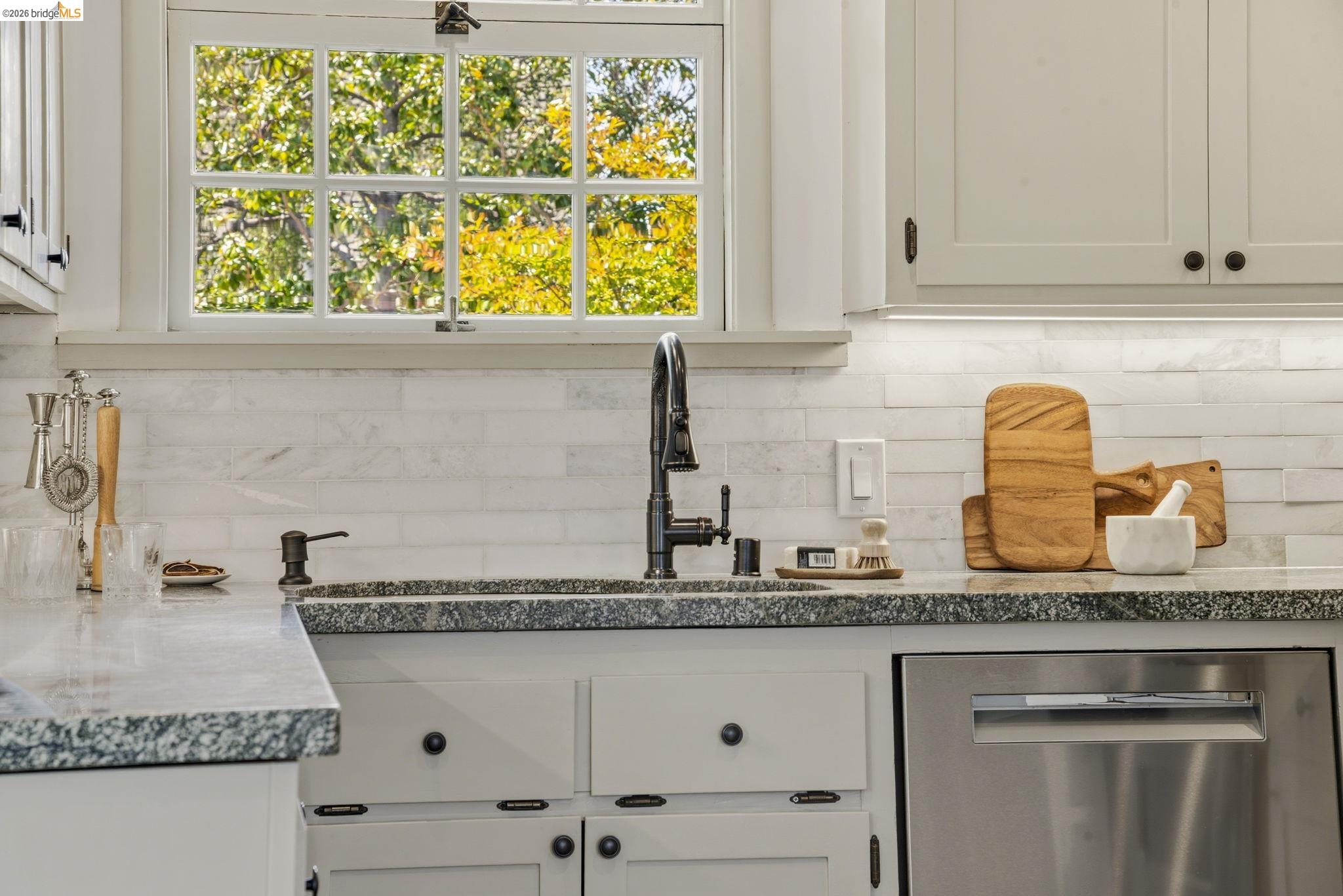 1087 Hubert Road Oakland, CA 94610 - Photo 12 of 67 Kitchen sink area featuring a multi-pane window, light-toned shaker cabinetry, dark speckled countertops, and a stacked white tile backsplash