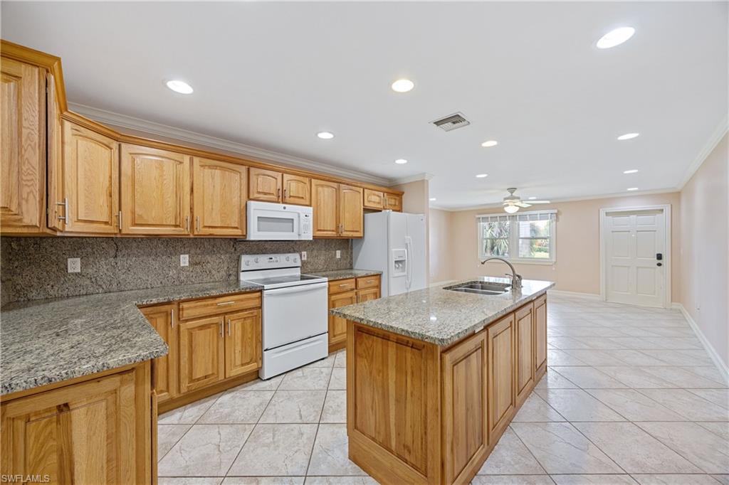 1120 Ridge Street Naples, FL 34103 - Photo 19 of 39 Kitchen featuring white appliances, crown molding, decorative backsplash, an island with sink, and light tile patterned floors.