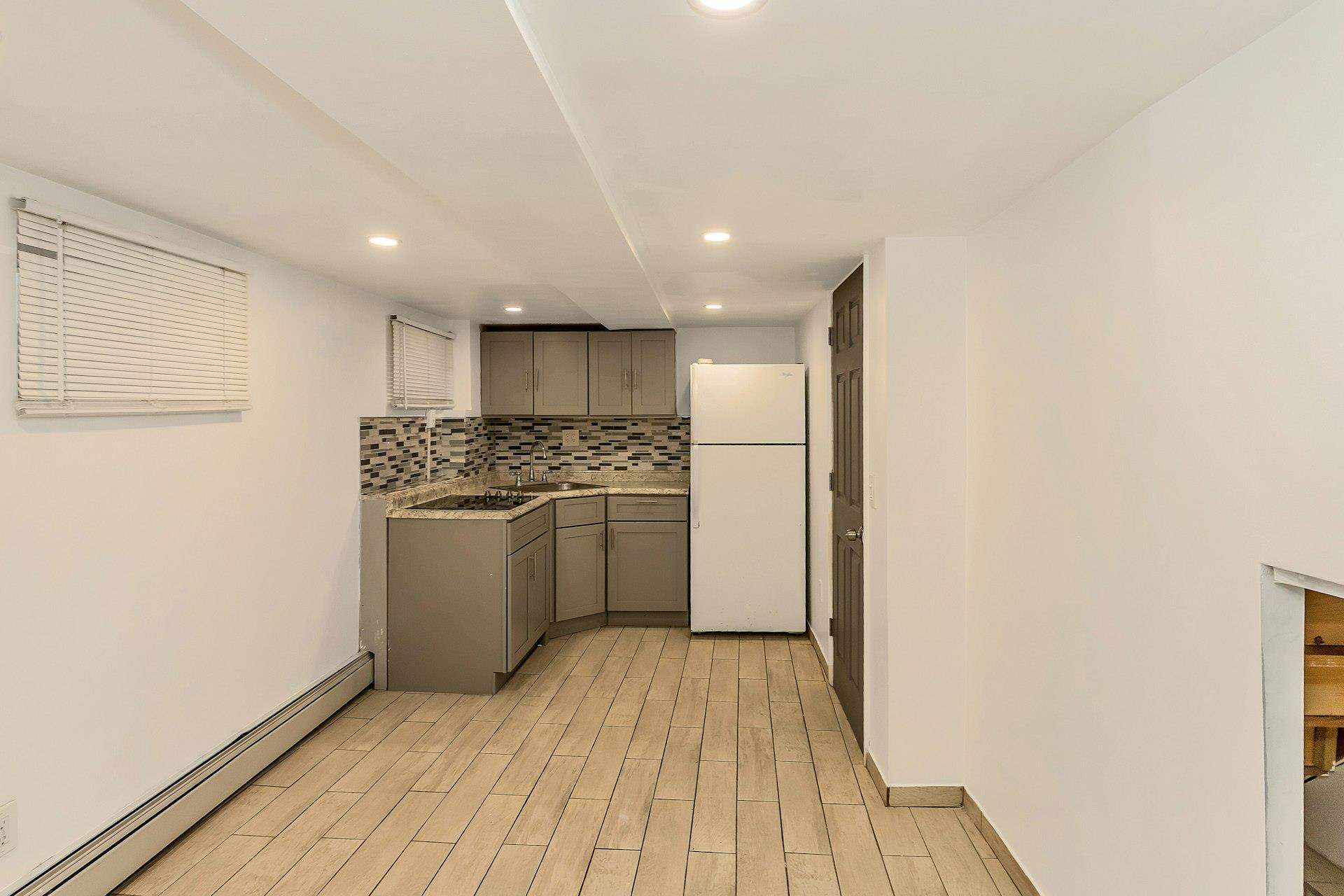 111-32 147th Street Queens, NY 11435 - Photo 18 of 24 Kitchen featuring decorative backsplash, gray cabinets, freestanding refrigerator, light wood finished floors, and a baseboard radiator