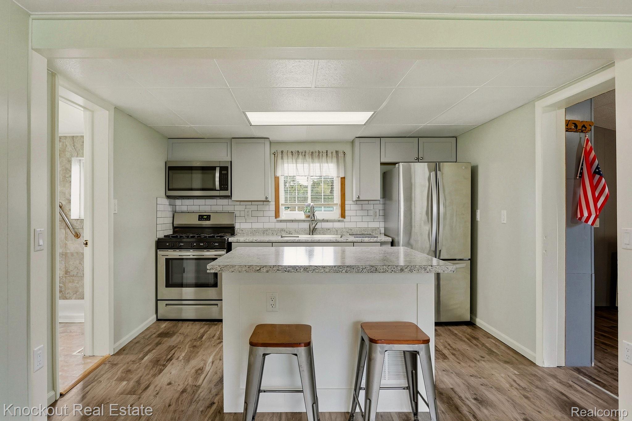 8771 Van Cleve Road Vassar, MI 48768 - Photo 14 of 44 Kitchen featuring wood-finish flooring, light cabinetry, stainless steel appliances, a subway tile backsplash, and a center island with a stone-finish countertop