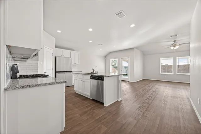 a kitchen with stainless steel appliances granite countertop wooden floors and white cabinets