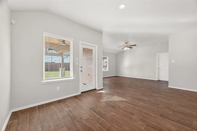 an empty room with wooden floor chandelier fan and windows