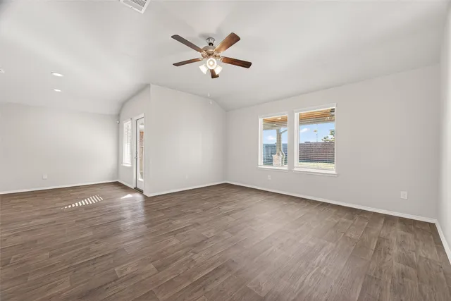 an empty room with wooden floor chandelier fan and windows