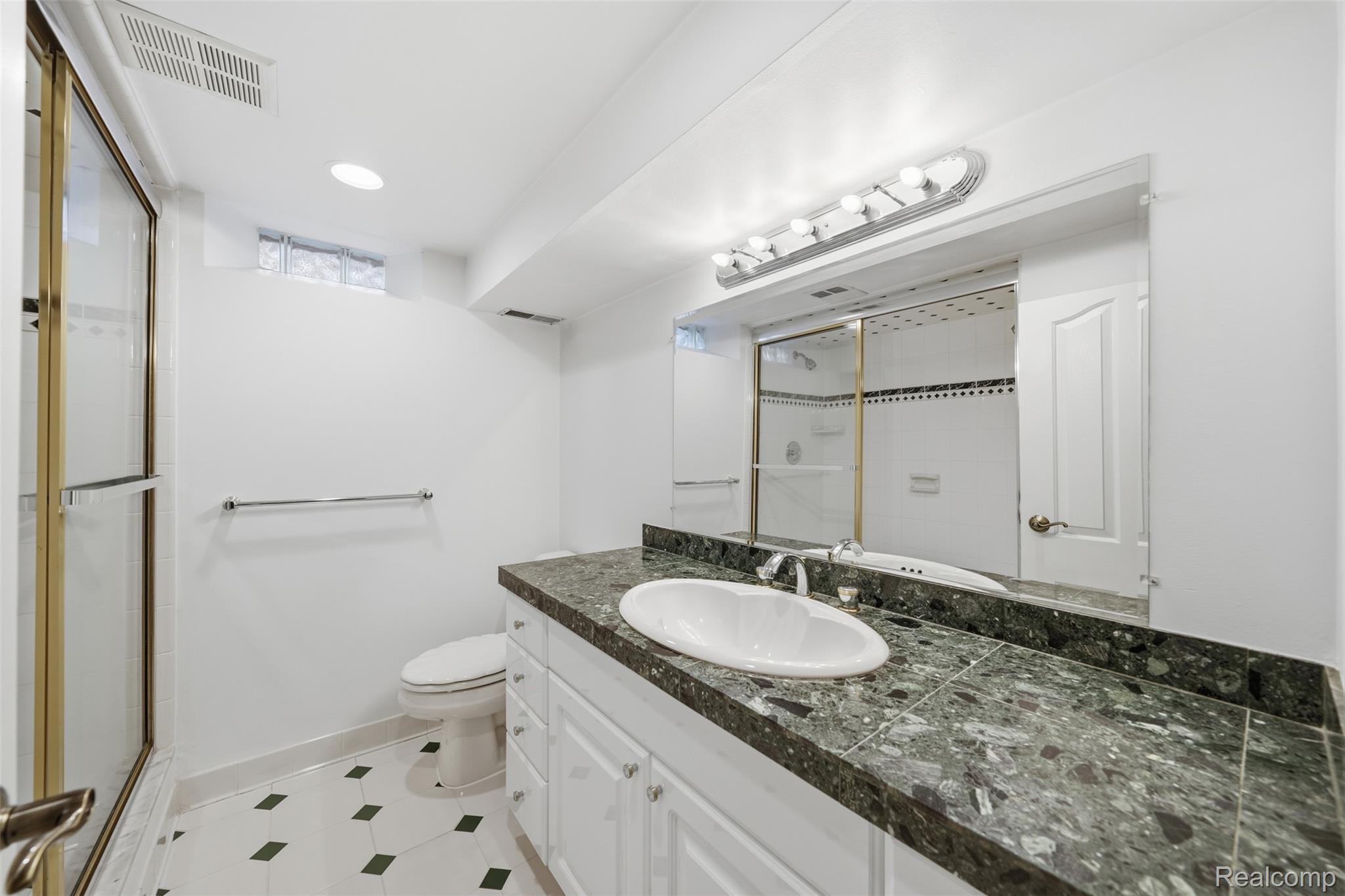 1087 Collingwood Drive Rochester, MI 48307 - Photo 50 of 56 Shower with a brass-finish frame, vanity with a dark speckled countertop, white vanity cabinetry, recessed lighting, and a patterned tile floor
