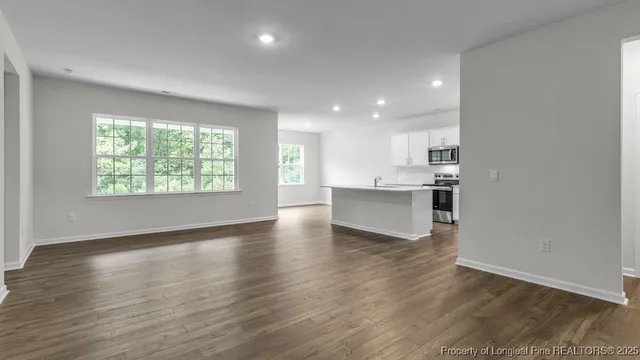 an empty room with wooden floor kitchen view and windows