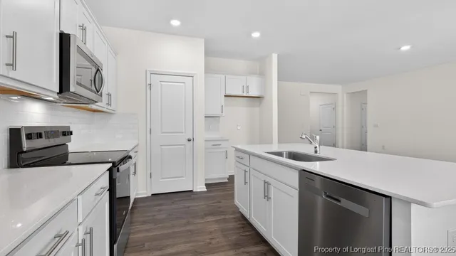 a kitchen with a sink dishwasher stove and white cabinets with wooden floor