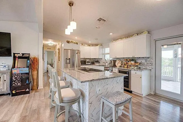 a kitchen with stainless steel appliances kitchen island granite countertop a stove a sink a refrigerator and white cabinets with wooden floor