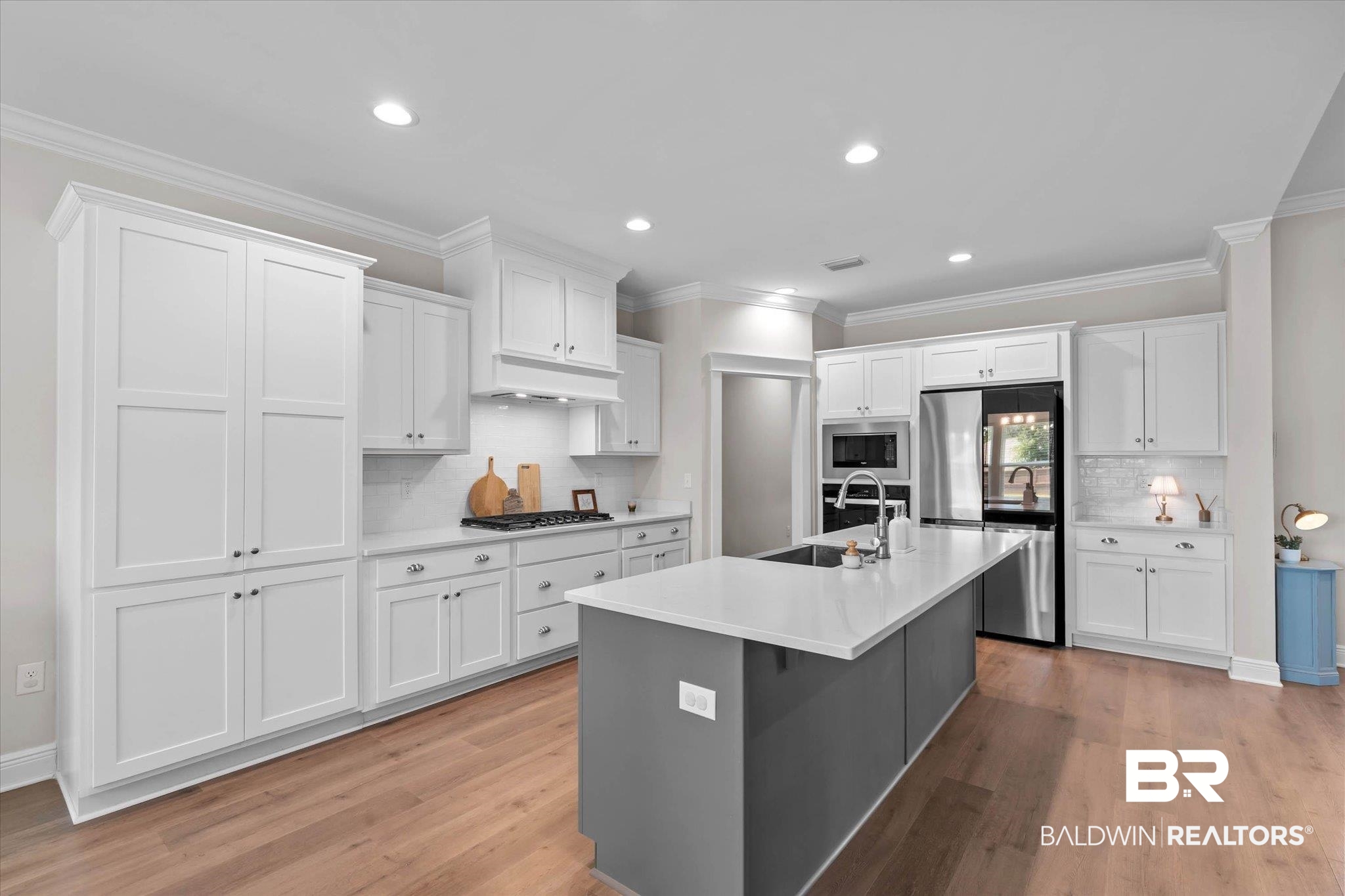 23523 Travis Stock Street Foley, AL 36535 - Photo 9 of 45 Expansive kitchen featuring white shaker cabinetry, stainless steel appliances, a large center island with a sink, quartz countertops, and wood-finish flooring