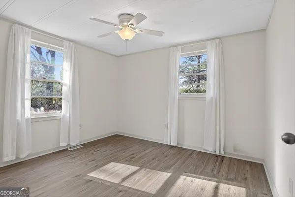 an empty room with wooden floor chandelier fan and windows