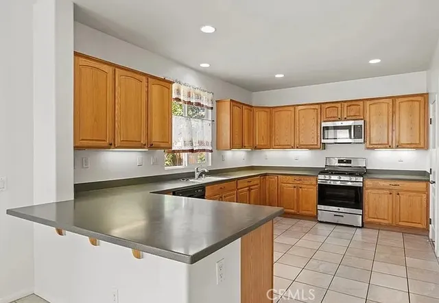 a kitchen with stainless steel appliances granite countertop a refrigerator a sink dishwasher a stove and white countertops with wooden floor