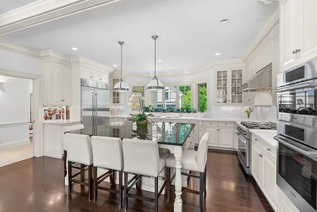 a kitchen with stainless steel appliances kitchen island granite countertop a stove a sink and white cabinets with wooden floor