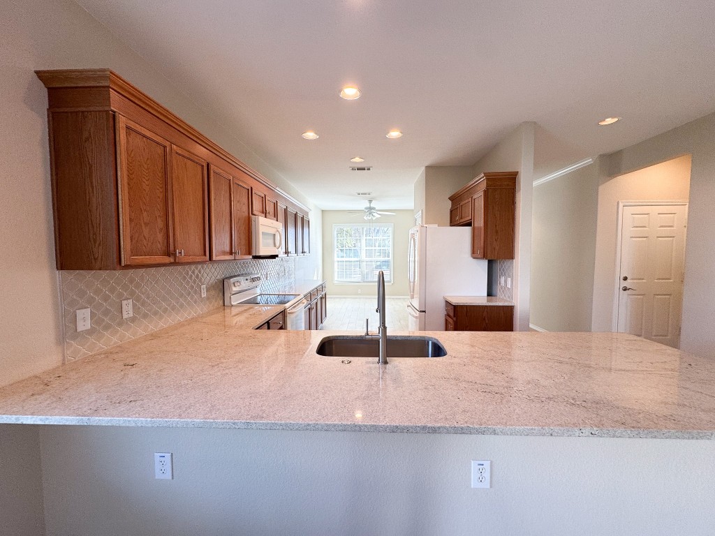 100 Sunbird Court Georgetown, TX 78633 - Photo 11 of 40 Kitchen with brown cabinetry, tasteful backsplash, white appliances, light stone counters, and a peninsula