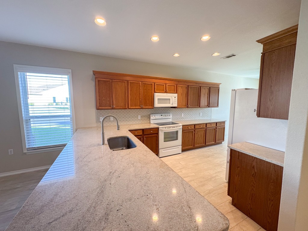 100 Sunbird Court Georgetown, TX 78633 - Photo 10 of 40 Kitchen featuring brown cabinets, tasteful backsplash, white appliances, recessed lighting, and light stone counters