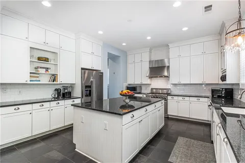 a kitchen with kitchen island granite countertop a sink a stove a refrigerator and white cabinets