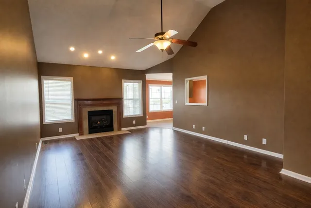 an empty room with wooden floor fireplace and windows
