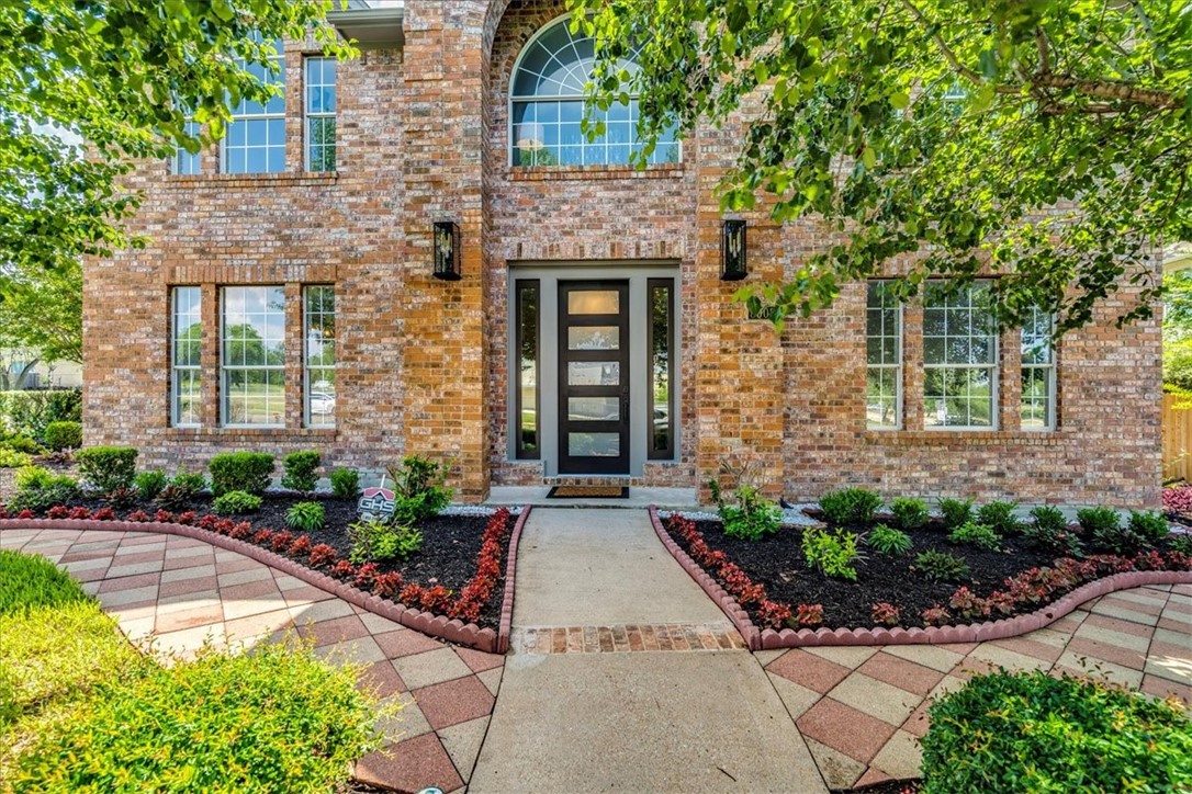 Walkway from the street surrounded by large tress and beautifully manicured lawn and flower gardens.
