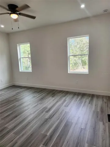 an empty room with wooden floor chandelier fan and windows