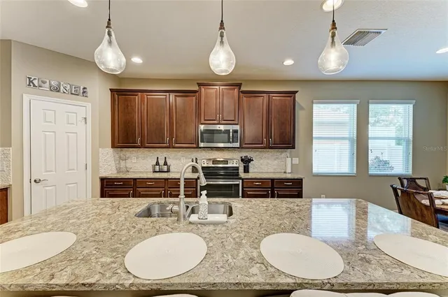 a kitchen with kitchen island granite countertop a sink a stove a dining table and chairs