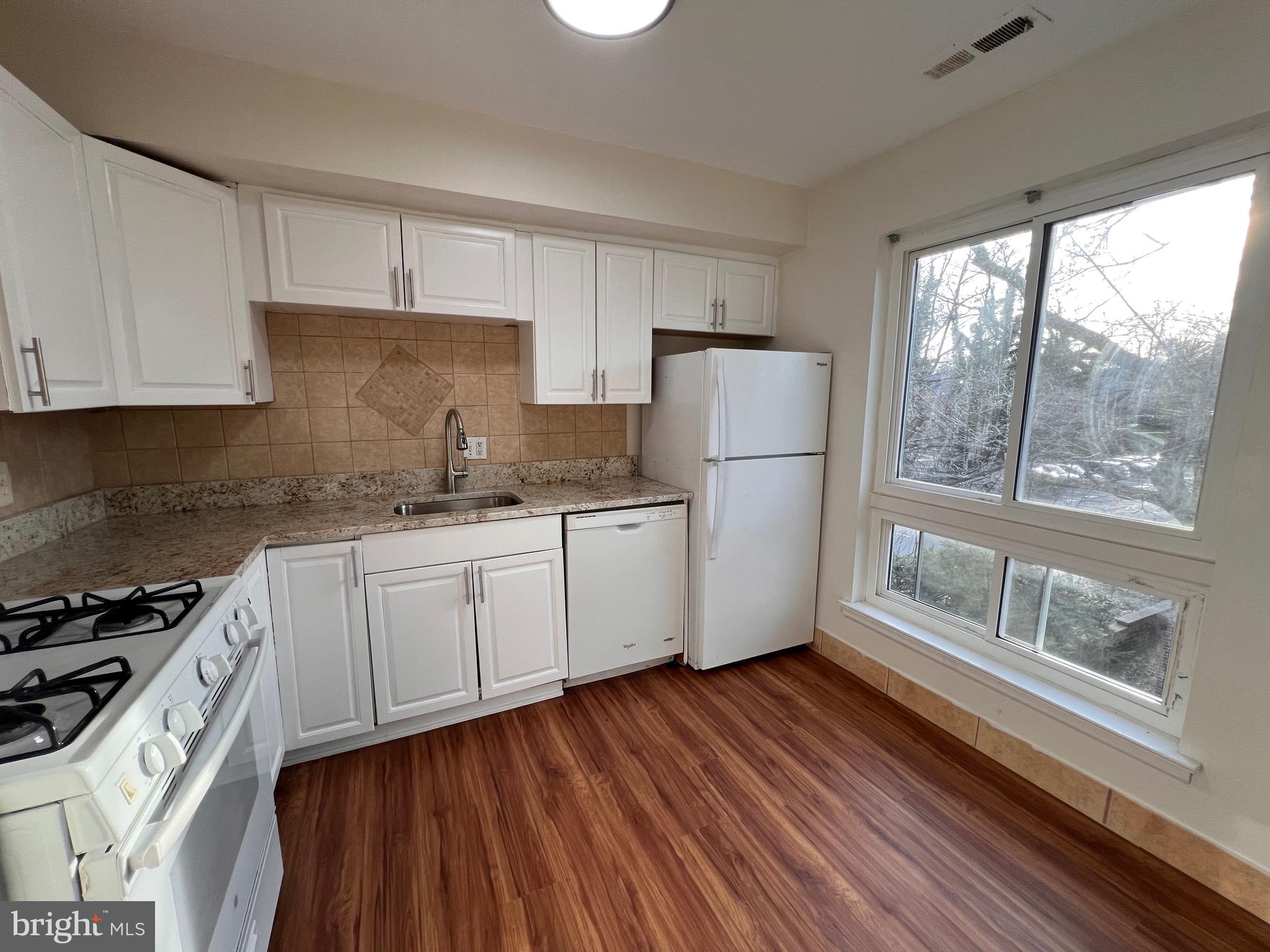 3964 Bel Pre Road, Unit 8 Silver Spring, MD 20906 - Photo 17 of 24 a kitchen with granite countertop a refrigerator a stove a sink and white cabinets with wooden floor