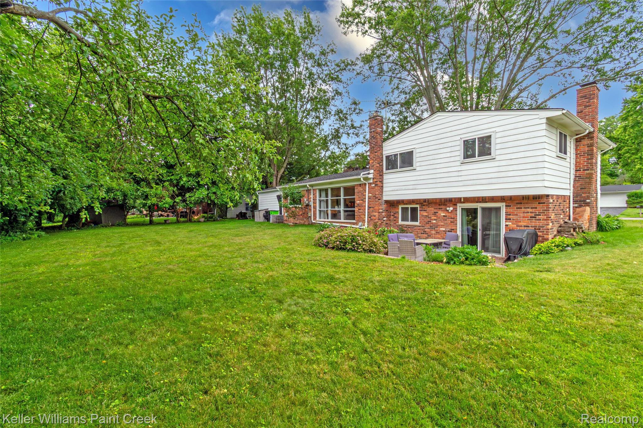 7093 Stonebrook Road West Bloomfield, MI 48322 - Photo 5 of 64 Expansive green lawn with mature trees and a two-story residence featuring brick and white siding