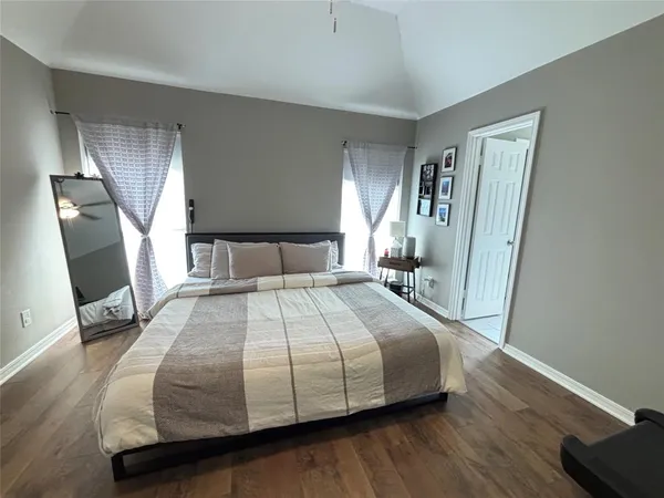 a bedroom with a bed a mirror on dresser and a wooden floor