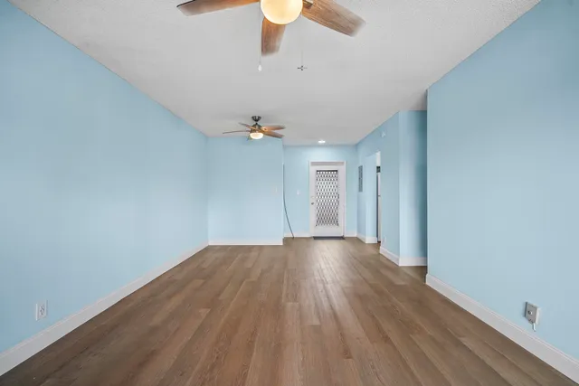 an empty room with wooden floor chandelier fan and windows